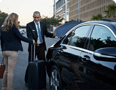 Professional chauffeur greeting a client beside a luxury black sedan.