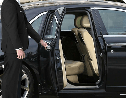 Chauffeur opening the rear door of a luxury vehicle for a passenger.